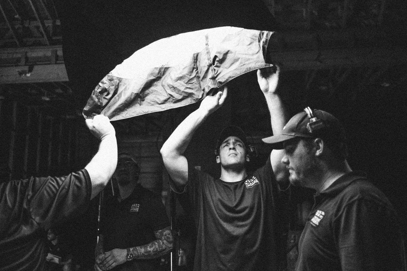Behind the scenes on INERTIA: grips raise a large silk overhead in a warehouse.