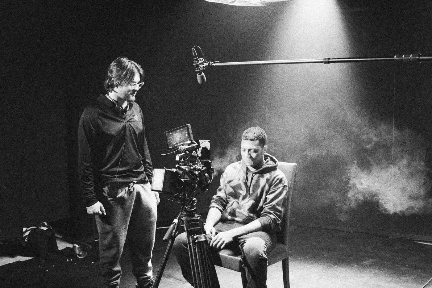 Behind the scenes on INERTIA: a camera operator stands beside his rig while an actor waits in a red chair, haze drifting behind them.