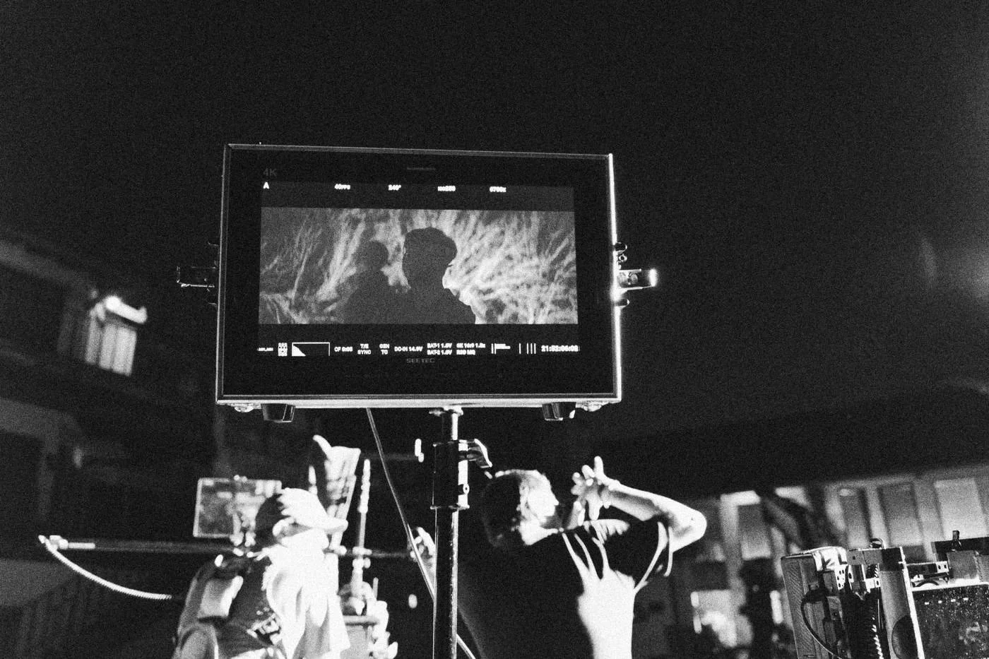 Behind the scenes on INERTIA: a field monitor on a stand shows the shot while crew work beneath it at night.