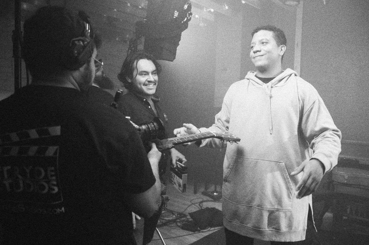 Behind the scenes on INERTIA: an actor in a gray hoodie grins at the crew filming him in a hazy studio.