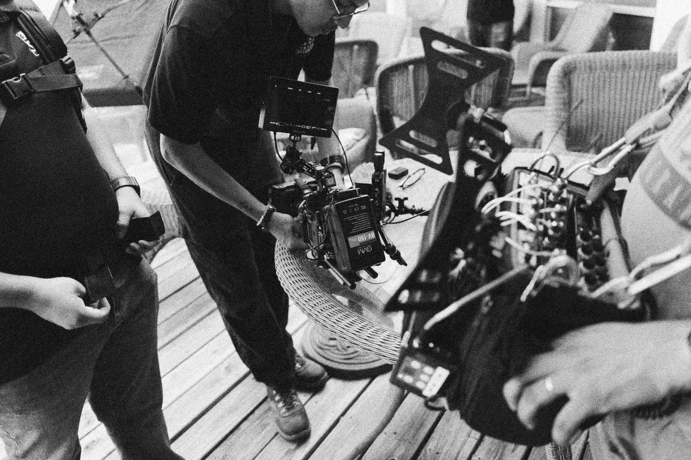 Behind the scenes on INERTIA: a camera operator rigs a camera on a wooden deck while crew hands hold cables and gear.
