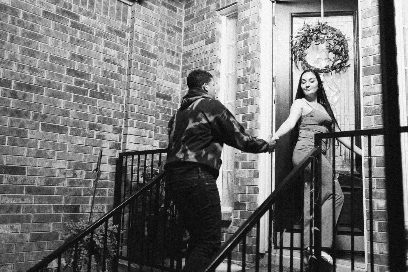 Behind the scenes on INERTIA: an actor takes an actress's hand at the front door of a brick house.