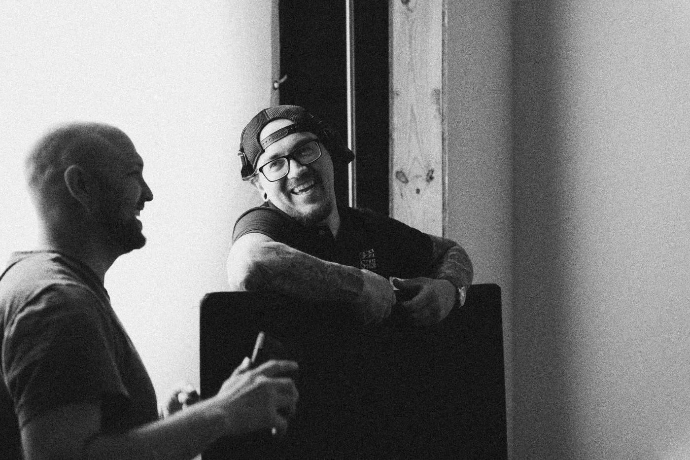 Behind the scenes on INERTIA: two crew members laugh together, one leaning over the back of a chair.