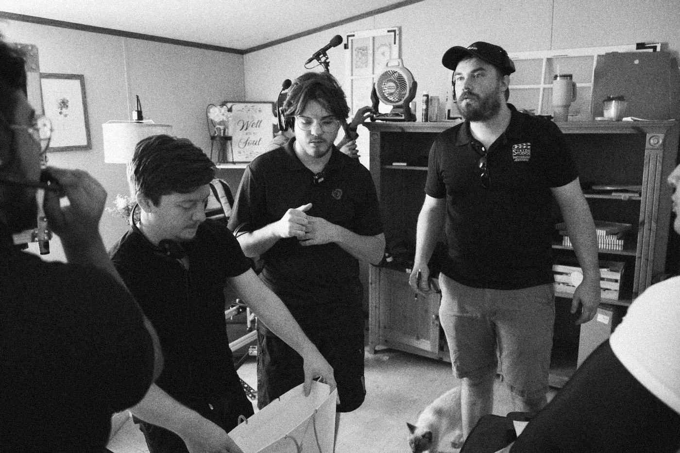 Behind the scenes on INERTIA: crew members stand in a living room set, one holding a white card.