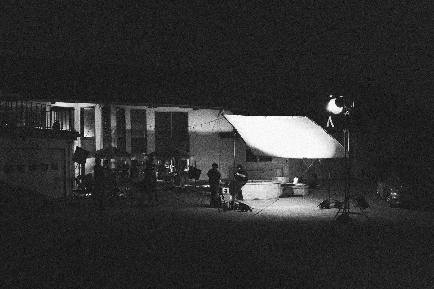 Behind the scenes on INERTIA: wide night view of a house exterior lit by one large soft light, crew small in the frame.
