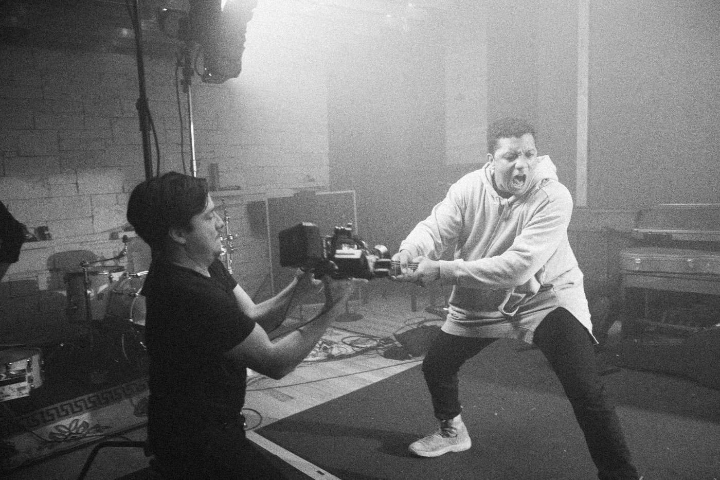 Behind the scenes on INERTIA: an actor lunges with a guitar while a camera operator films him at close range.