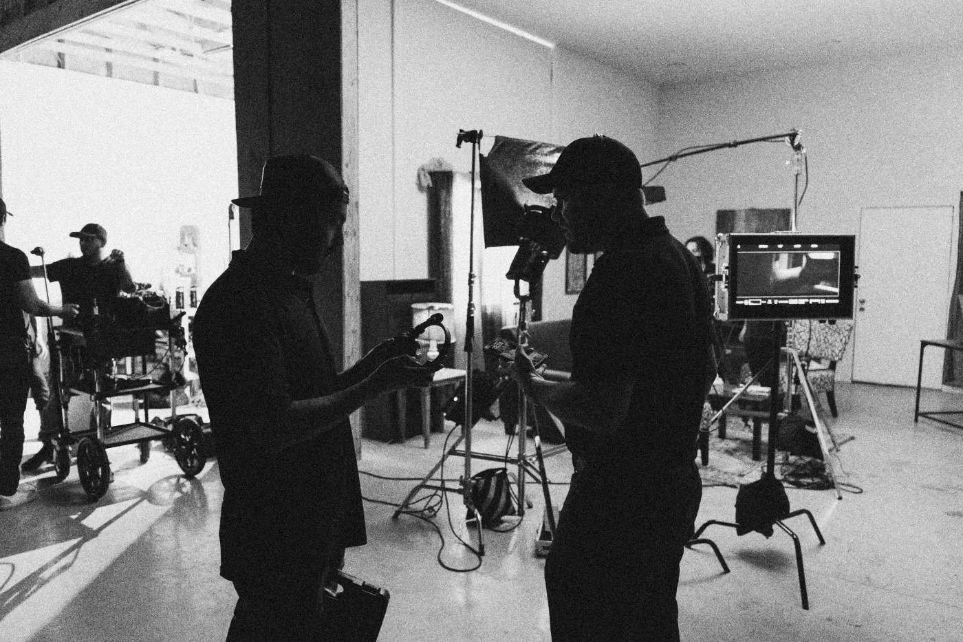 Behind the scenes on INERTIA: crew members set up a camera, monitor and lights on a living room set.