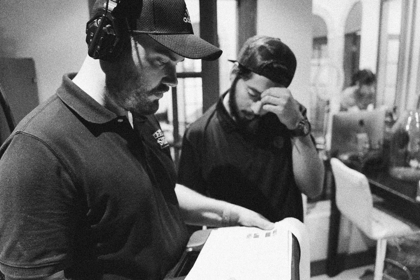 Behind the scenes on INERTIA: two crew members in headsets look down at paperwork on set.