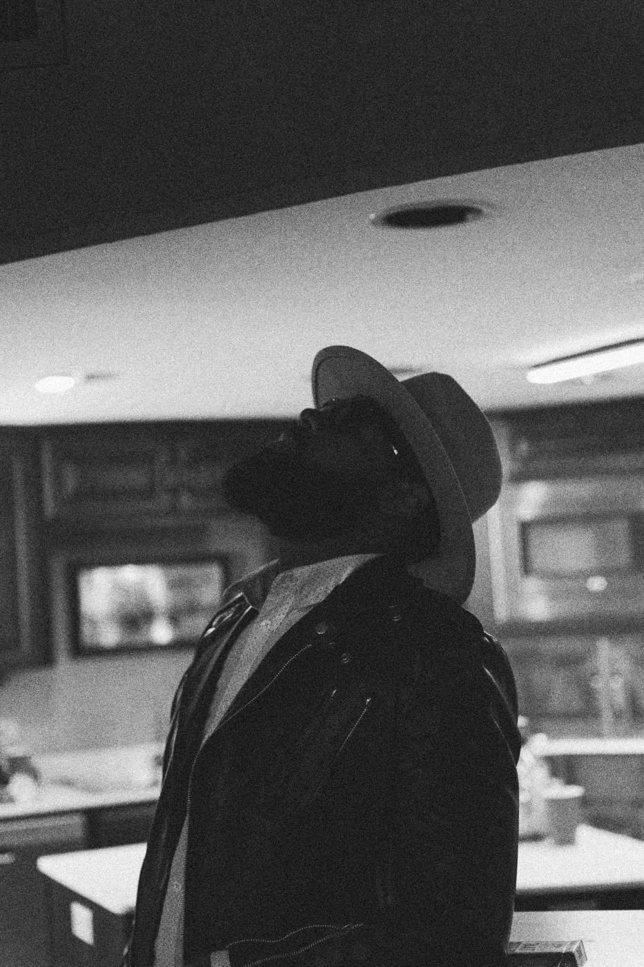 Behind the scenes on INERTIA: an actor in a hat and leather jacket looking up in a kitchen set.