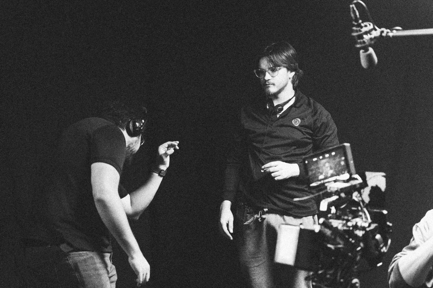 Behind the scenes on INERTIA: a camera operator carrying a rig walks past a crew member who gestures toward him.