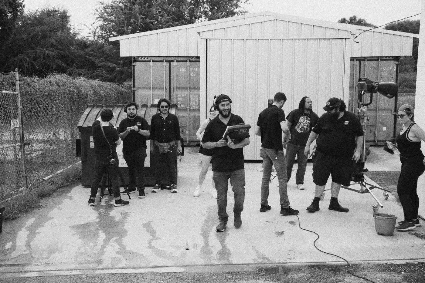 Behind the scenes on INERTIA: the whole crew stands together outside a metal building on a wet concrete lot.