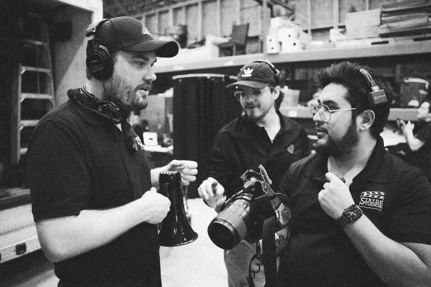 Behind the scenes on INERTIA: three crew members in caps and headsets talk, one holding a camera with a long lens.