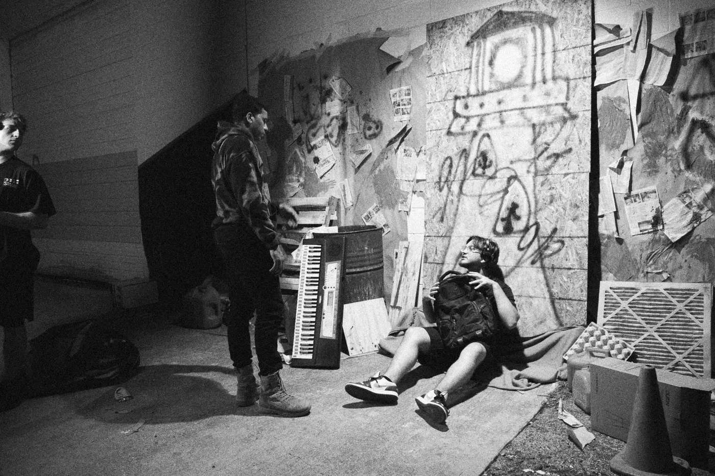 Behind the scenes on INERTIA: crew stand around an actor lying on a green blanket before the graffiti set at night.