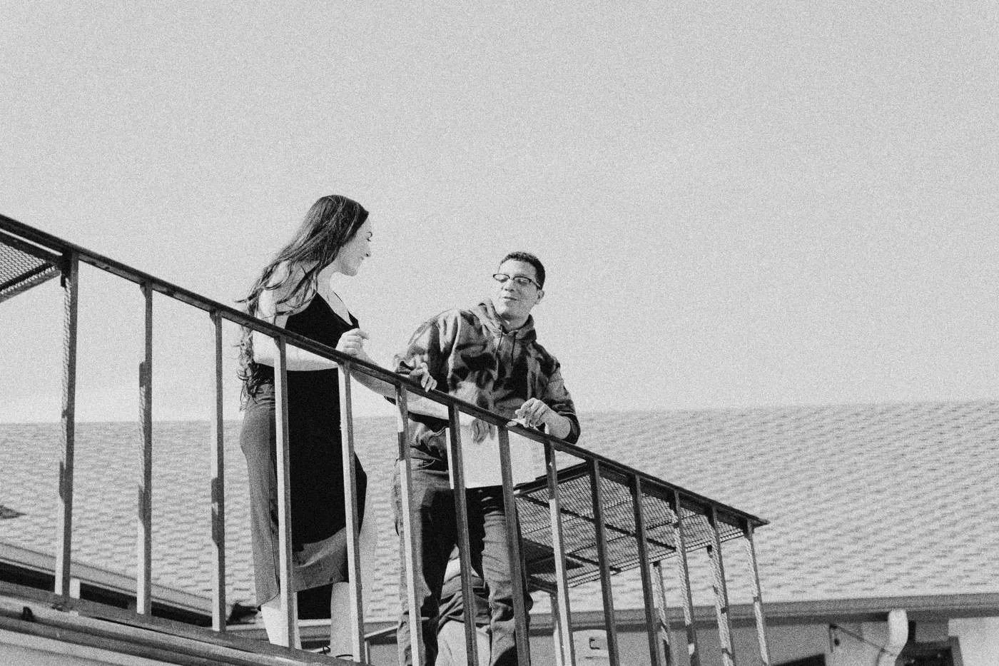 Behind the scenes on INERTIA: two actors stand at a railing on an exterior staircase against a bright sky.