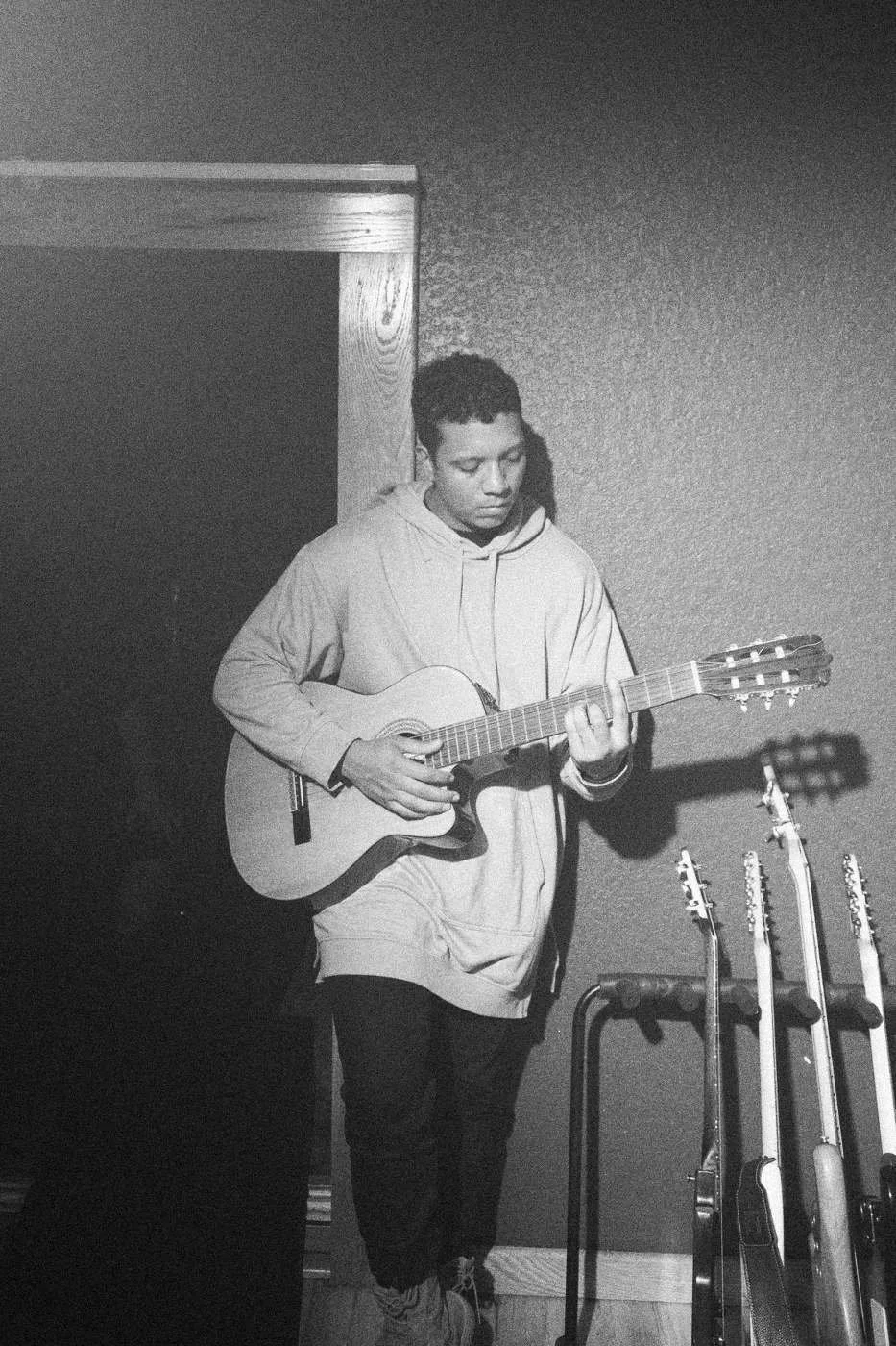 Behind the scenes on INERTIA: an actor playing an acoustic guitar beside a rack of guitars.