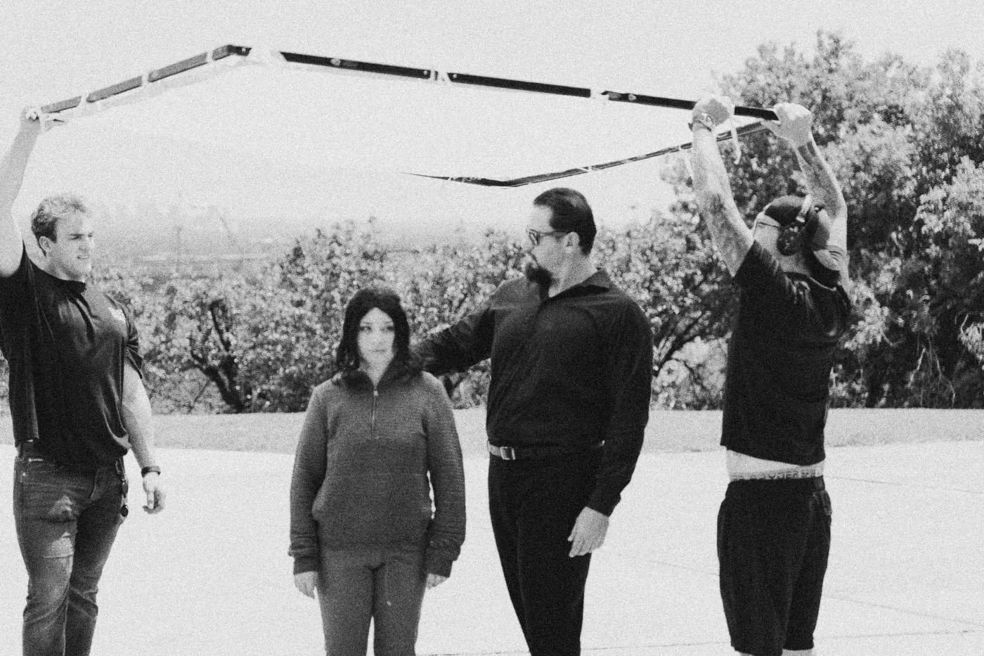 Behind the scenes on INERTIA: crew members hold a large diffusion frame over two actors on a hilltop driveway in daylight.
