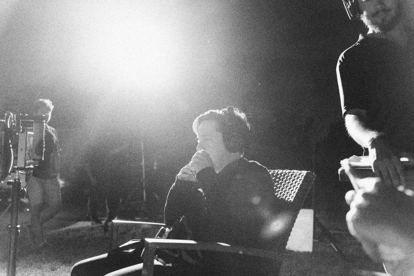 Behind the scenes on INERTIA: an actor sits in a chair under a blazing light that flares across the frame at night.