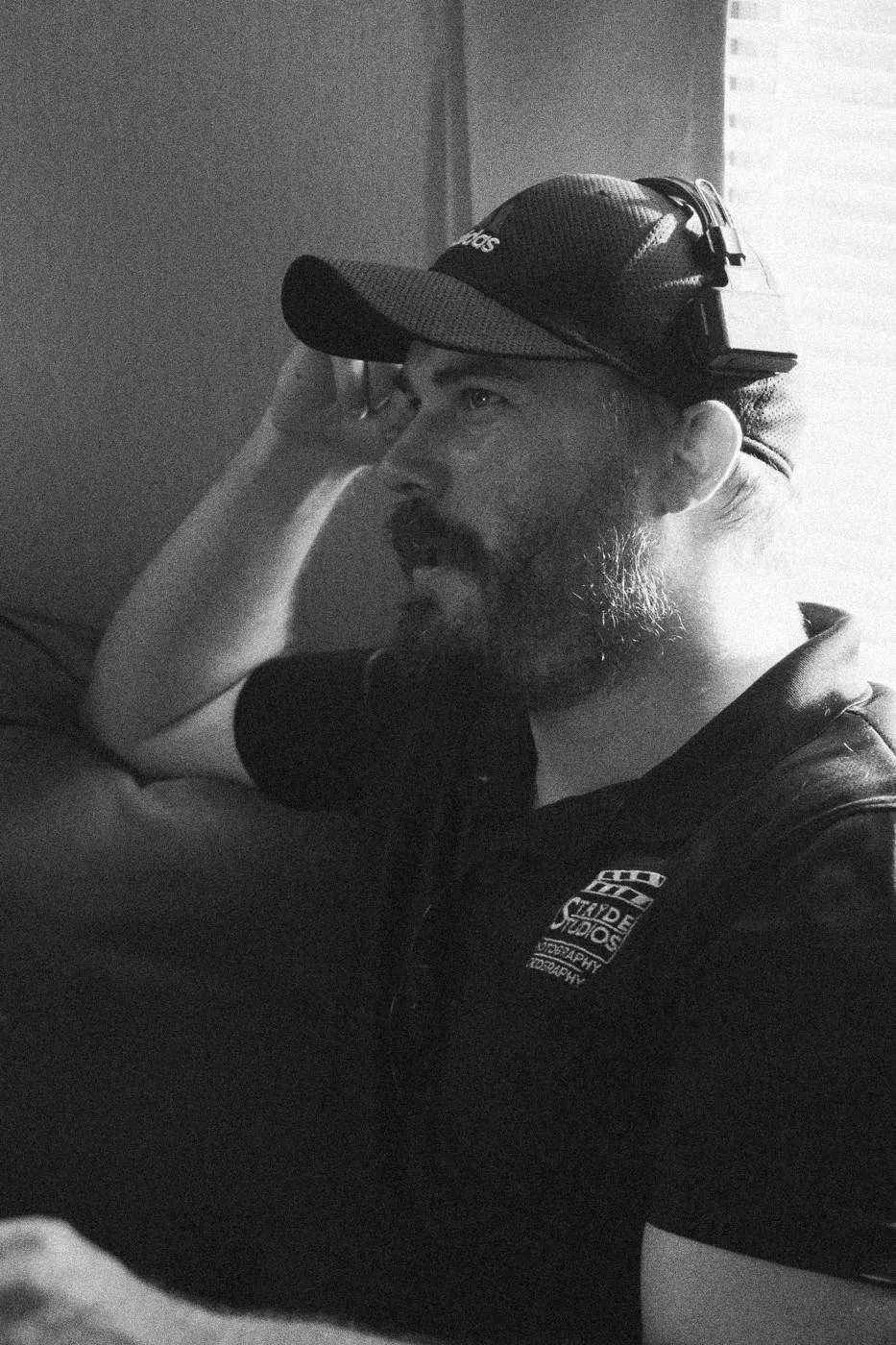 Behind the scenes on INERTIA: a crew member in a cap and headset sitting on a couch, hand at his head.