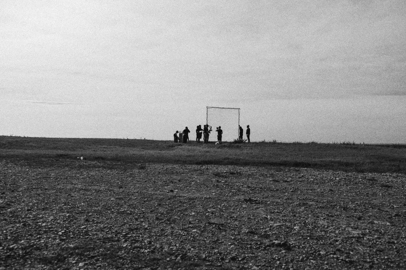 Behind the scenes on INERTIA: a flat field under a heavy gray sky with a small group of crew around a frame far off.
