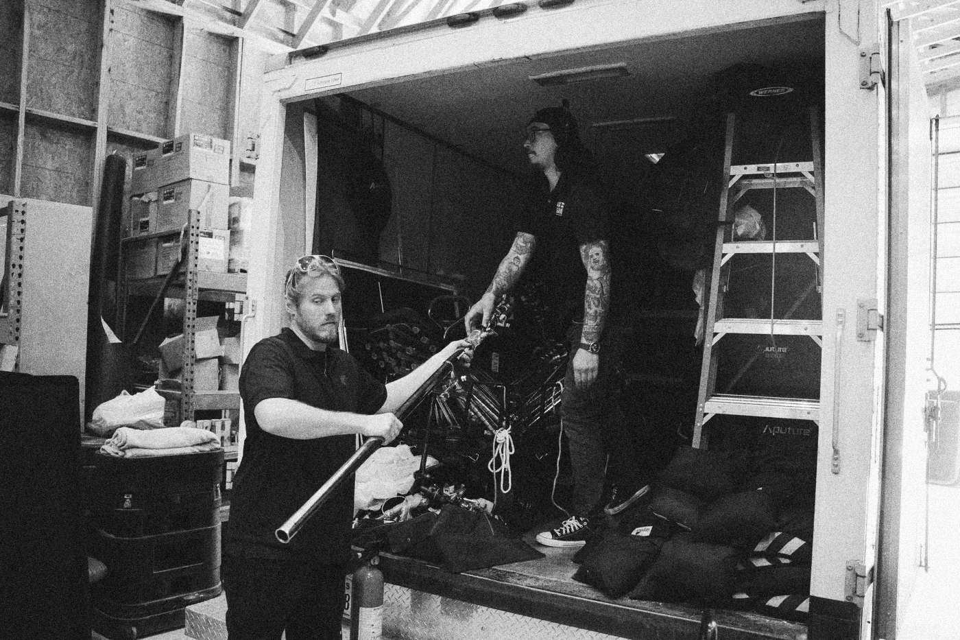 Behind the scenes on INERTIA: two crew members unload grip gear from the back of an equipment truck inside a warehouse.