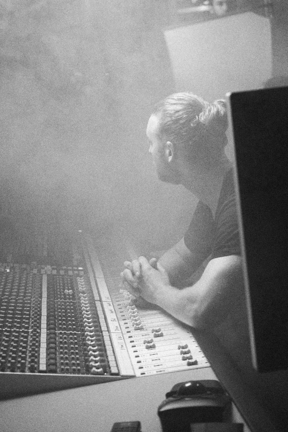 Behind the scenes on INERTIA: a man leaning on a mixing console in haze.