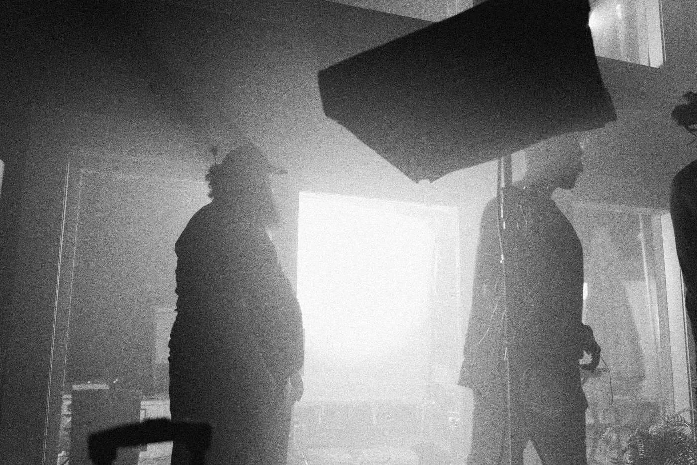 Behind the scenes on INERTIA: two crew members stand in silhouette before a bright soft light box in blue haze.