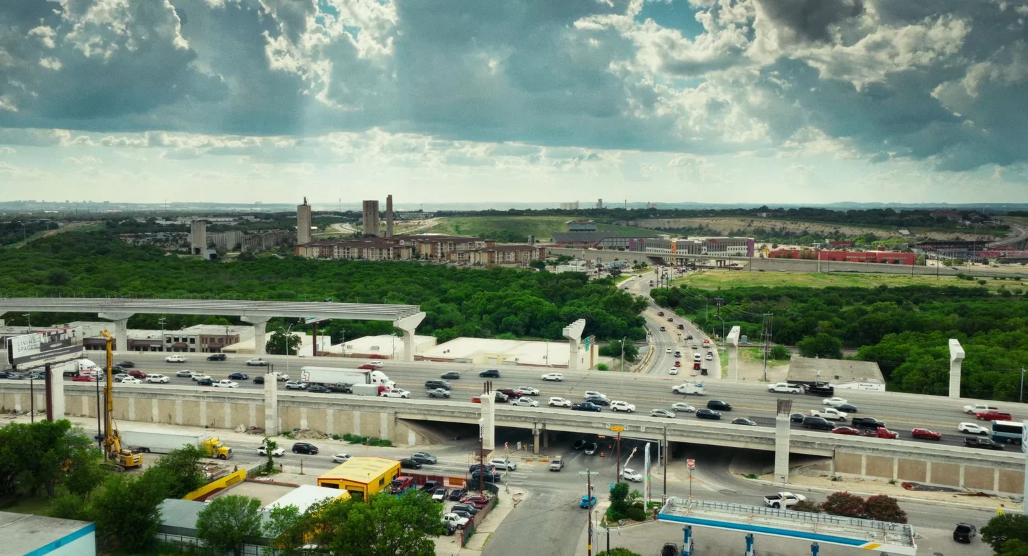 Still from INERTIA: an aerial view of a busy elevated highway and interchange with a distant skyline.