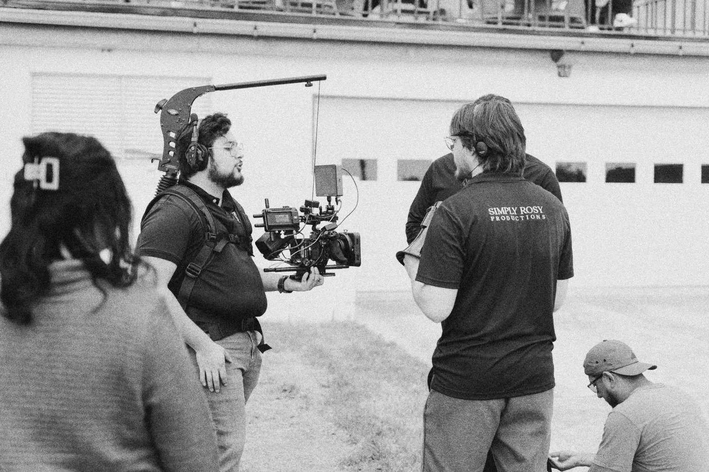Behind the scenes on INERTIA: a camera operator with a rigged camera and crew members talk in a driveway outside a white garage.