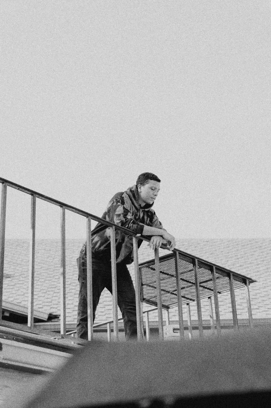 Behind the scenes on INERTIA: an actor leaning on a staircase railing against a white sky.