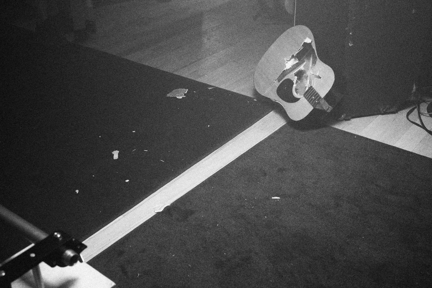 Behind the scenes on INERTIA: an acoustic guitar lies on a dark floor beside tape marks.