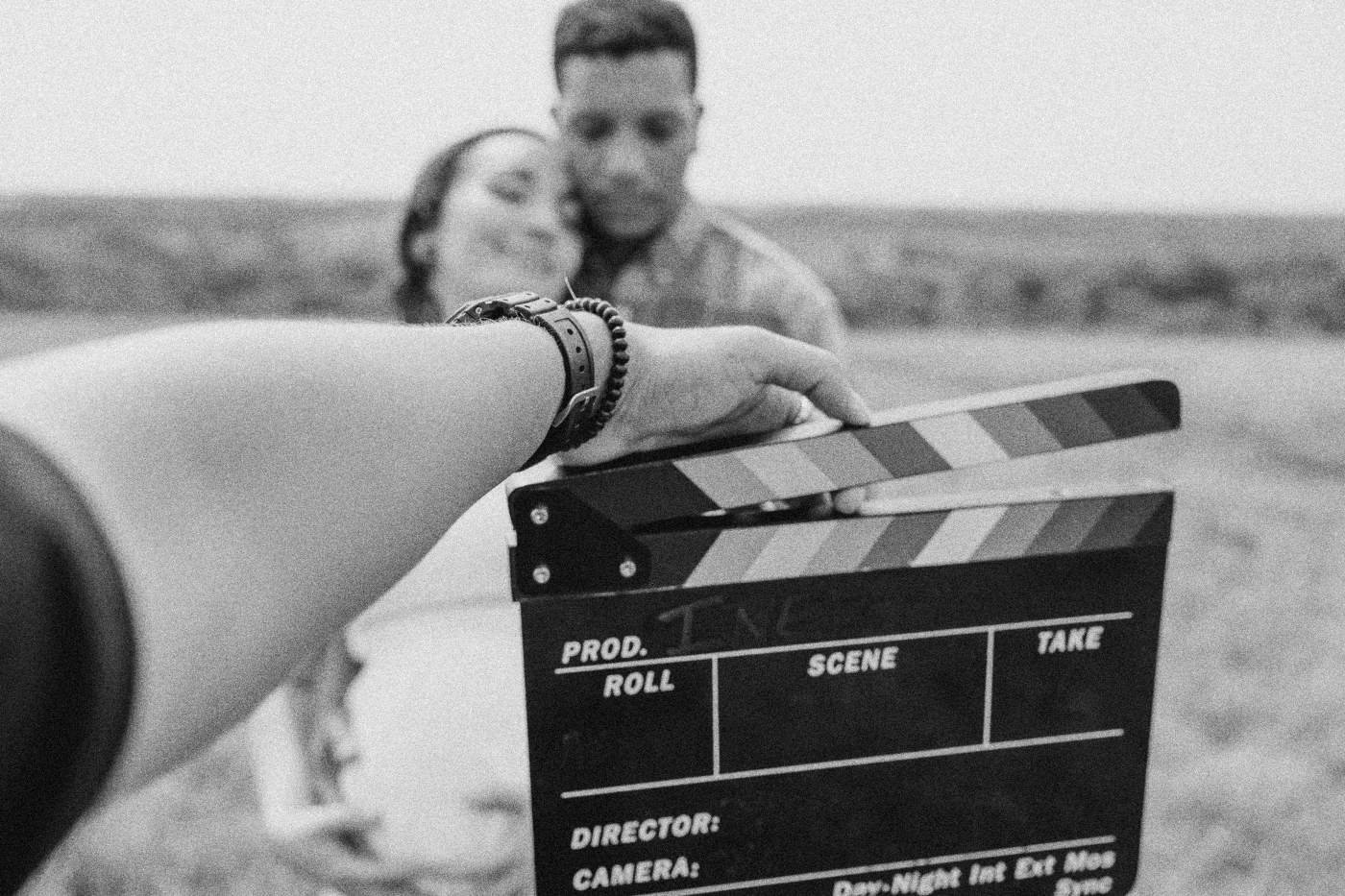 Behind the scenes on INERTIA: a hand holds up the slate in front of two actors embracing in a field.
