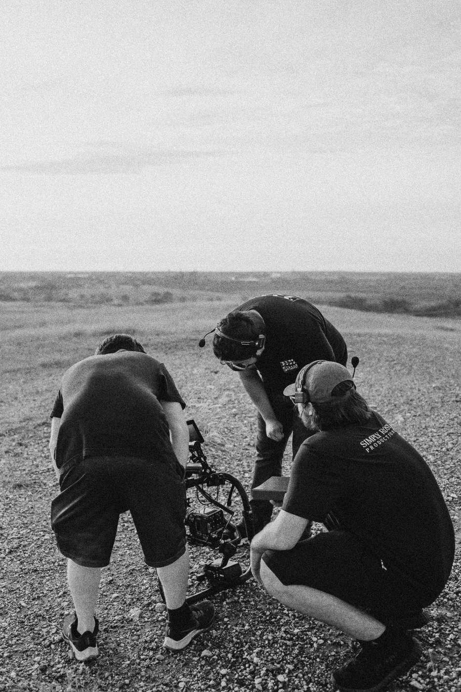 Behind the scenes on INERTIA: crew members crouching to adjust gear on a gravel hilltop.