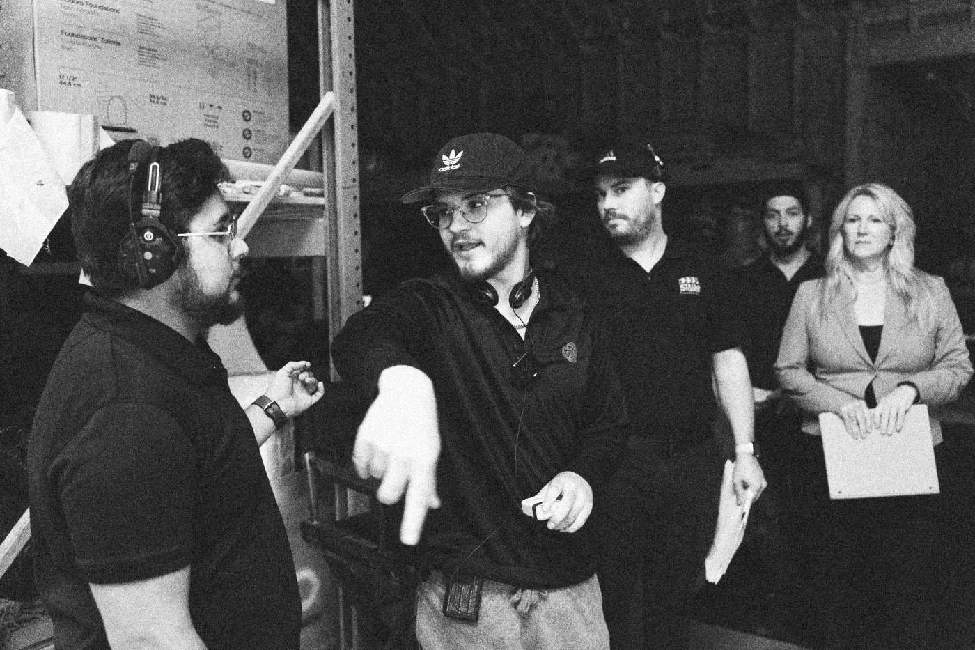 Behind the scenes on INERTIA: a crew member points while giving directions to a small group in a warehouse, one holding papers.
