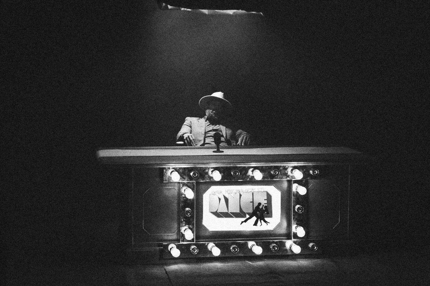 Behind the scenes on INERTIA: wide view of the lit desk under a single spotlight, surrounded by dark studio space.