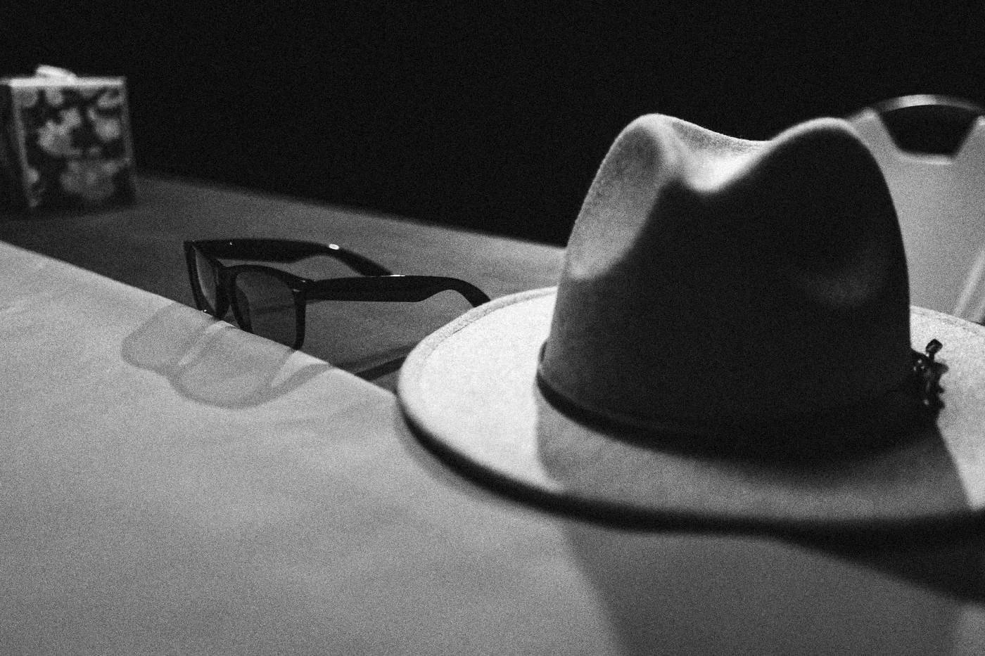 Behind the scenes on INERTIA: detail of a gray hat and sunglasses resting on a pink table edge.