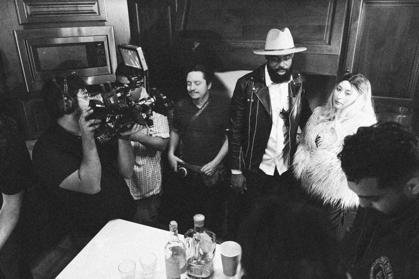 Behind the scenes on INERTIA: a camera operator films cast members gathered around a kitchen island with drinks.