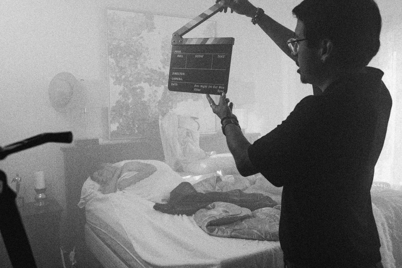 Behind the scenes on INERTIA: a crew member holds up the slate over a bed in teal light.