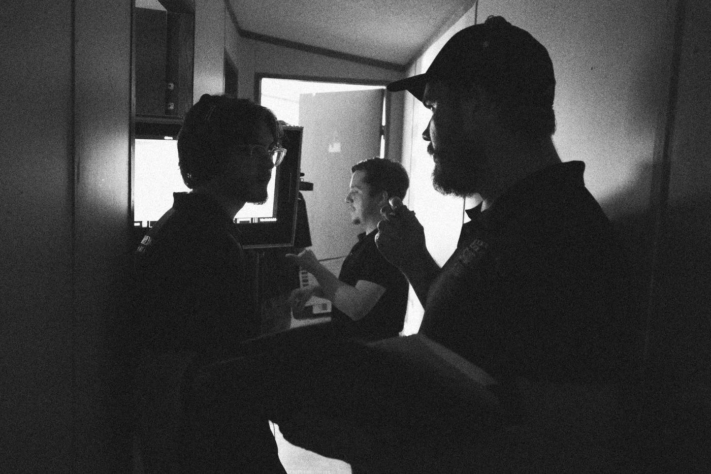 Behind the scenes on INERTIA: crew members in silhouette watch a small monitor in a dark hallway.