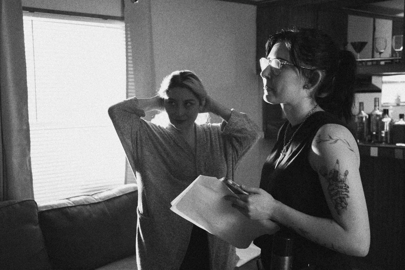 Behind the scenes on INERTIA: two women talk in a living room, one holding script pages.