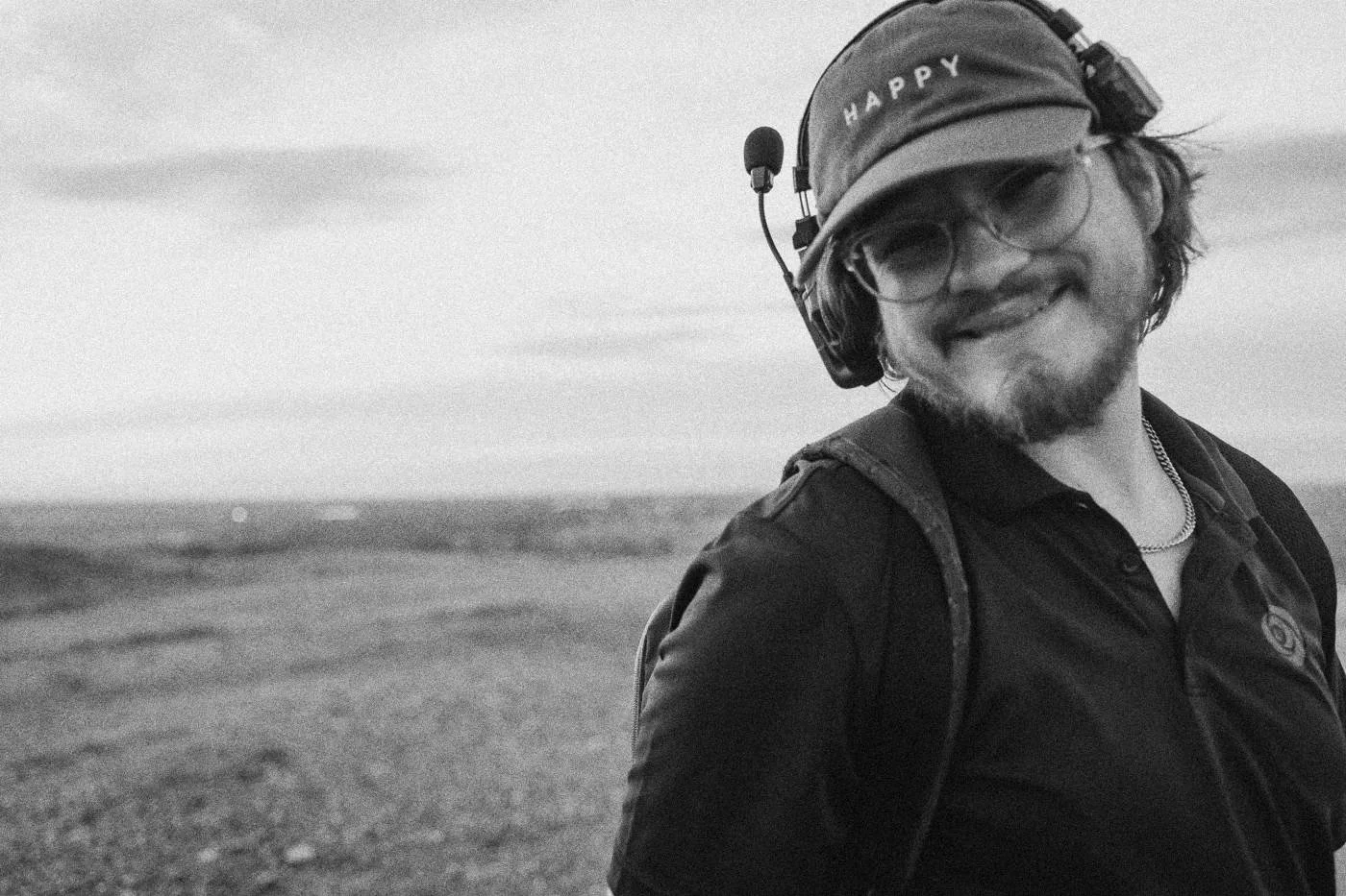 Behind the scenes on INERTIA: a smiling crew member in a cap and headset looks at the camera on a hilltop.