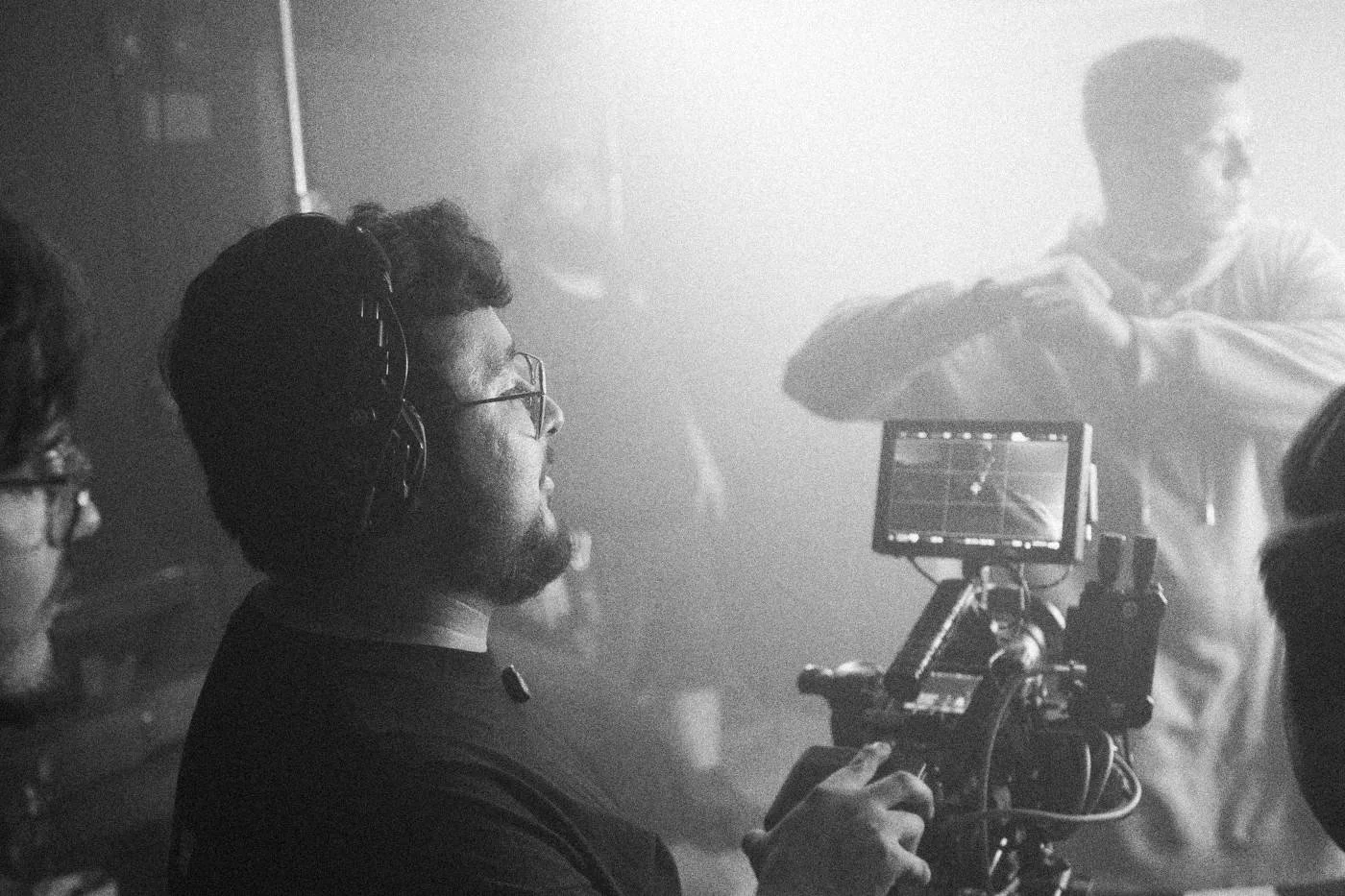 Behind the scenes on INERTIA: a camera operator checks his monitor in haze while an actor stands behind him.