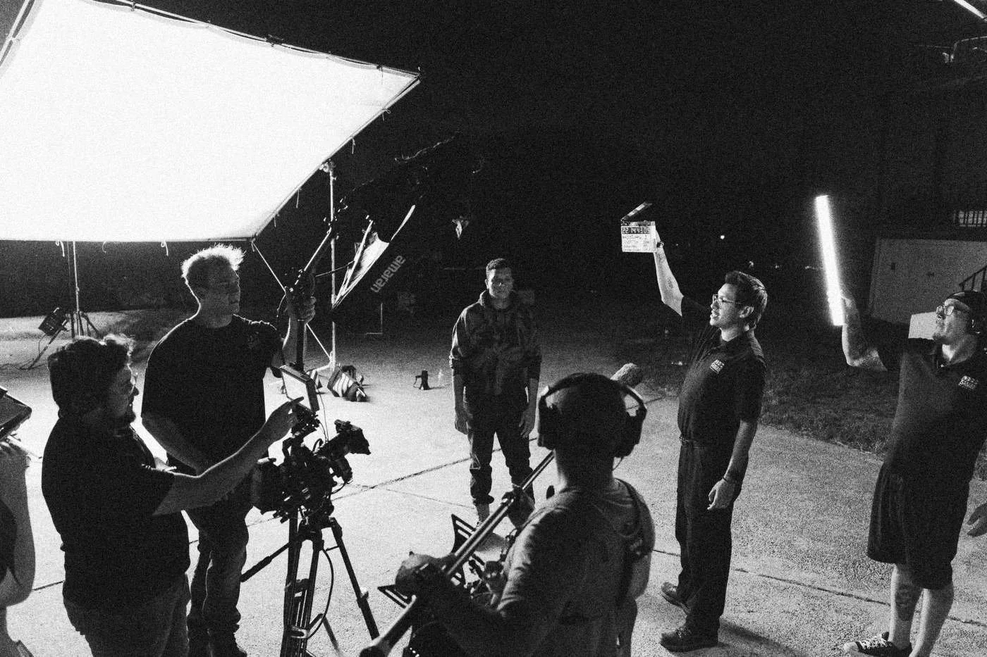 Behind the scenes on INERTIA: the crew gathers on a dark driveway under a large soft light, one holding up a slate.
