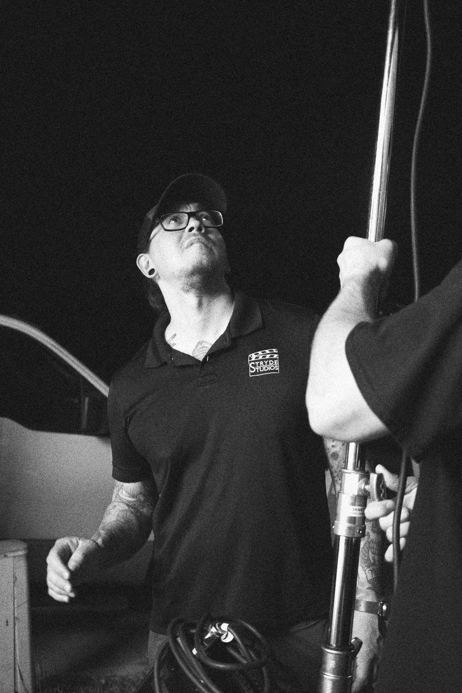 Behind the scenes on INERTIA: a crew member looking up while steadying a light stand at night.