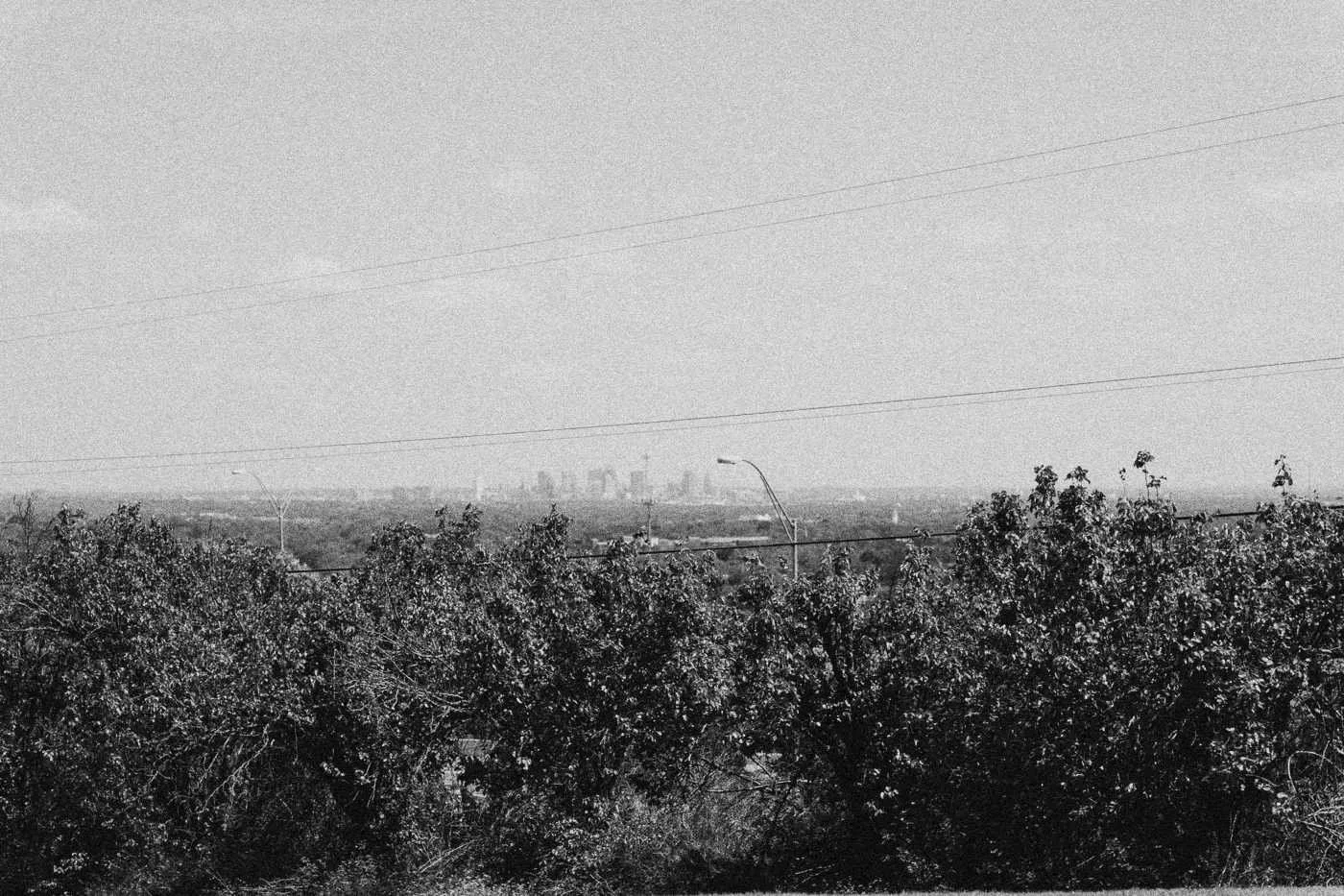 Behind the scenes on INERTIA: a wide hilltop view over trees toward a distant city skyline under a pale sky.