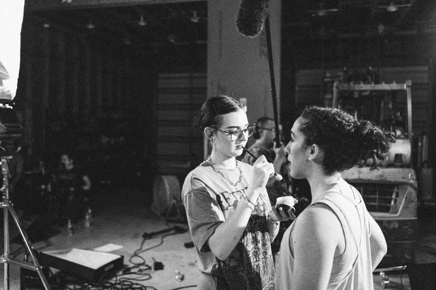 Behind the scenes on INERTIA: a makeup artist touches up an actress in a warehouse studio.