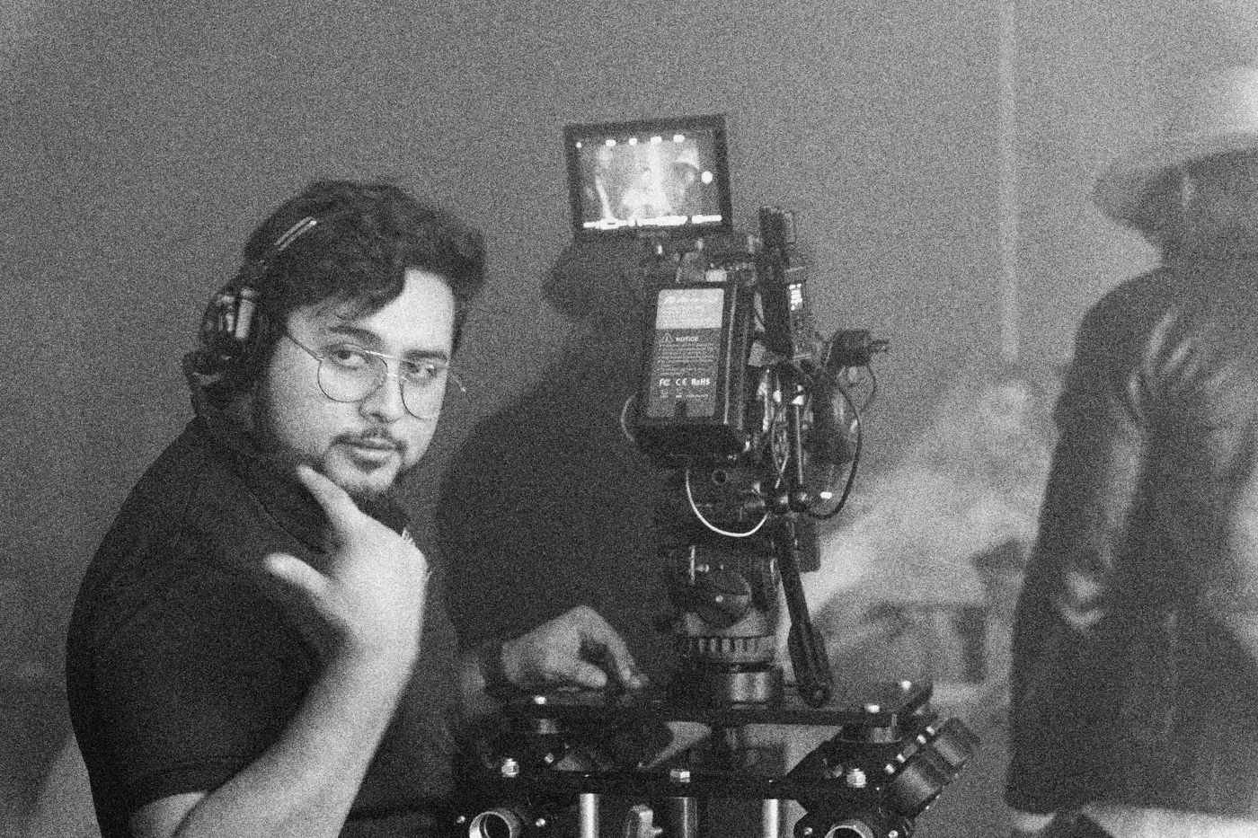 Behind the scenes on INERTIA: a camera operator with a headset rests his hand at his chin beside a rigged camera in haze.