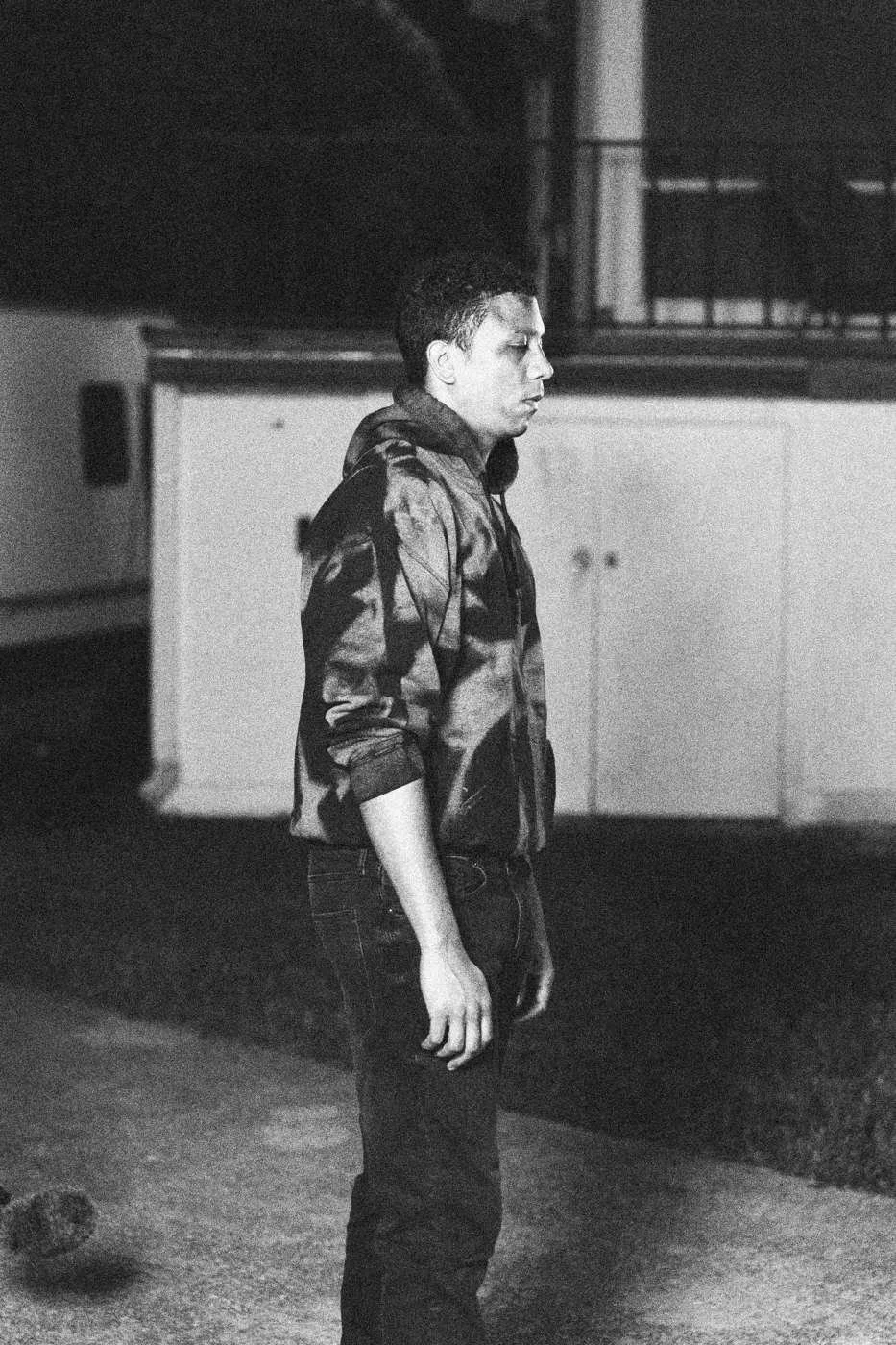 Behind the scenes on INERTIA: an actor in a dark jacket standing on grass outside a trailer at dusk.