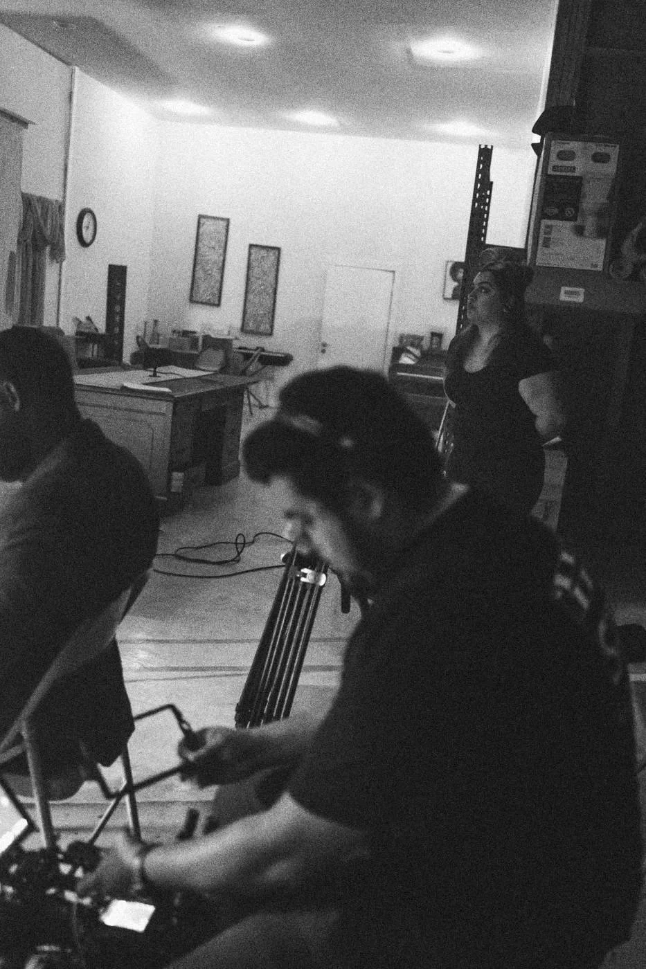 Behind the scenes on INERTIA: a camera operator seated at his rig in a long room.