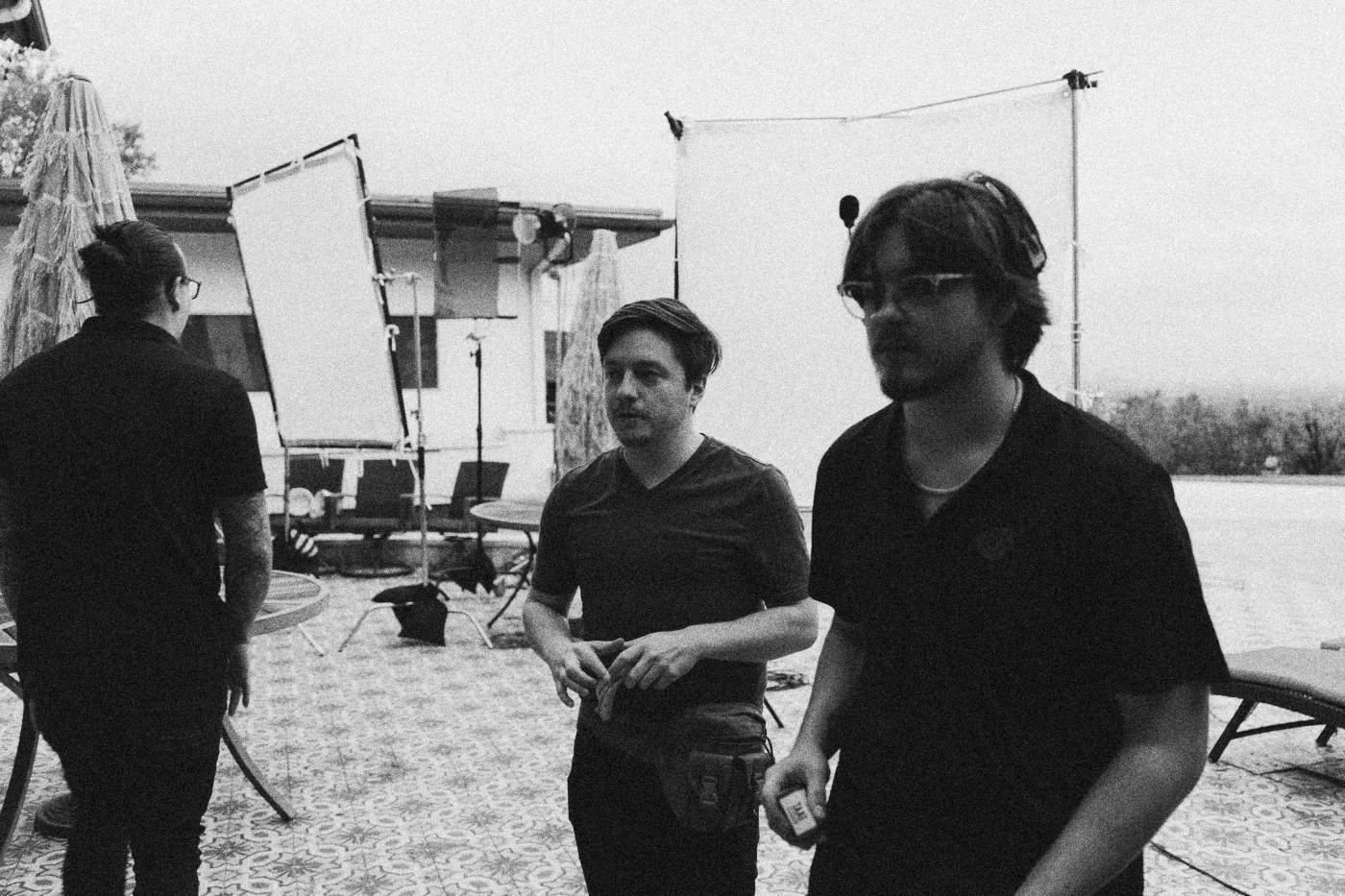 Behind the scenes on INERTIA: crew members stand on a patio outside a house with reflectors and a diffusion frame set up behind them.