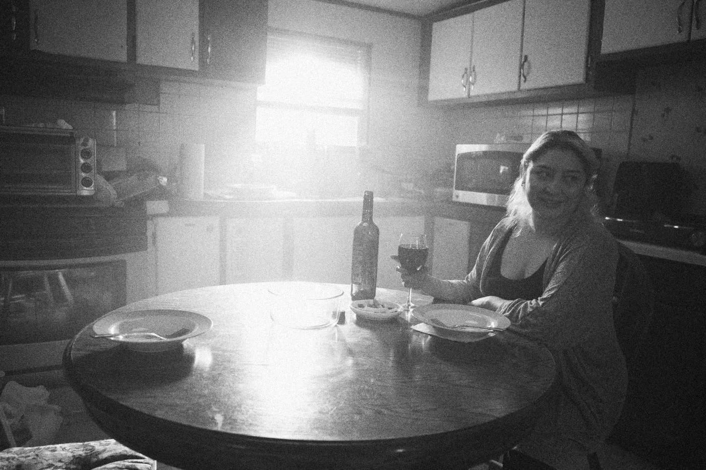 Behind the scenes on INERTIA: an actress sits at a round kitchen table with a glass of wine, sunlight pouring through the window behind.